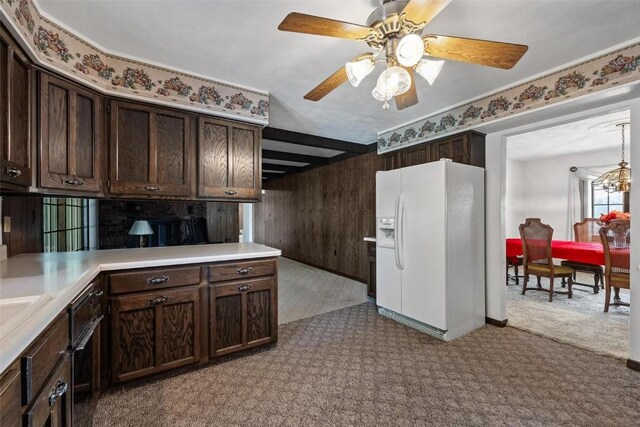 kitchen with wooden walls, ceiling fan with notable chandelier, white refrigerator with ice dispenser, dark brown cabinets, and light countertops