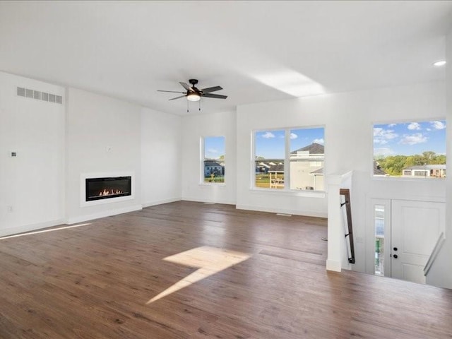 unfurnished living room featuring visible vents, a glass covered fireplace, ceiling fan, wood finished floors, and baseboards