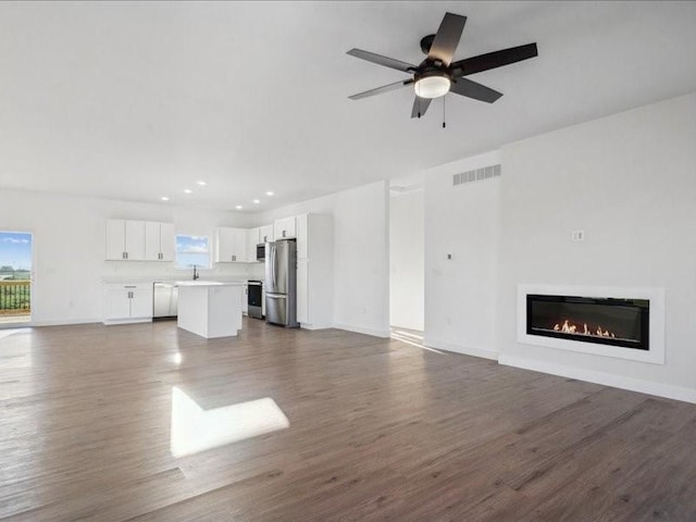 unfurnished living room featuring a wealth of natural light, dark wood-style flooring, a glass covered fireplace, and visible vents
