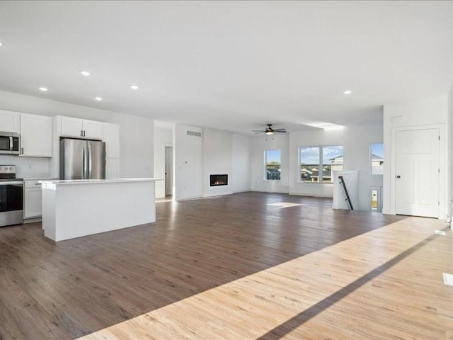 unfurnished living room featuring ceiling fan, a warm lit fireplace, recessed lighting, wood finished floors, and visible vents