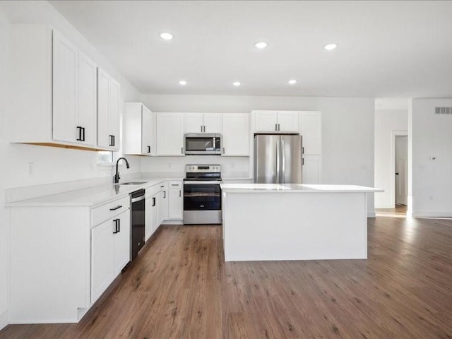 kitchen with wood finished floors, a kitchen island, a sink, white cabinetry, and appliances with stainless steel finishes