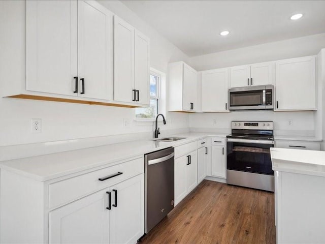 kitchen featuring dark wood-style flooring, stainless steel appliances, light countertops, white cabinetry, and a sink