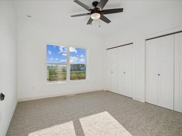unfurnished bedroom featuring baseboards, carpet floors, ceiling fan, and multiple closets