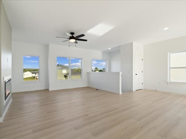 unfurnished living room with light wood-style floors, a glass covered fireplace, baseboards, and a ceiling fan