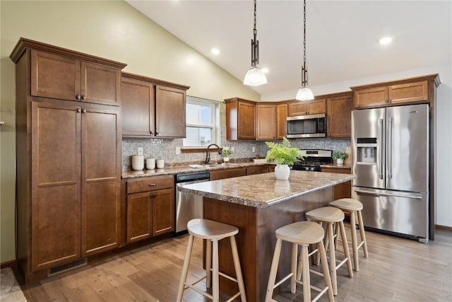 kitchen with a sink, a kitchen island, visible vents, appliances with stainless steel finishes, and a kitchen bar