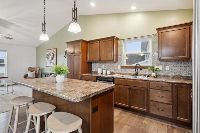 kitchen featuring light wood finished floors, a breakfast bar area, a center island, vaulted ceiling, and a sink