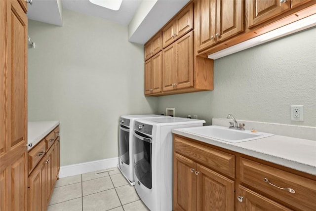 clothes washing area featuring cabinet space, baseboards, washing machine and clothes dryer, a sink, and light tile patterned flooring