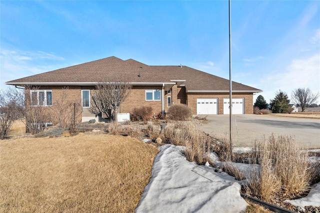 single story home with an attached garage, roof with shingles, concrete driveway, and brick siding