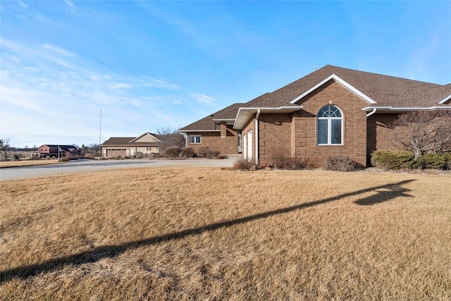 view of front of property featuring concrete driveway, brick siding, roof with shingles, and a front yard