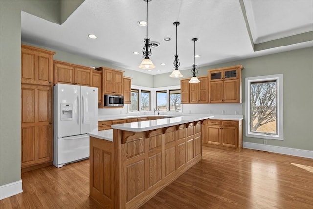 kitchen featuring white refrigerator with ice dispenser, light countertops, a center island, light wood finished floors, and stainless steel microwave