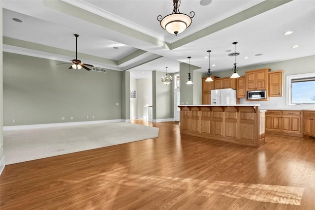 kitchen featuring a tray ceiling, stainless steel microwave, light wood-style floors, white fridge with ice dispenser, and baseboards