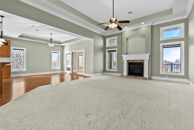 unfurnished living room with baseboards, a raised ceiling, crown molding, and a glass covered fireplace