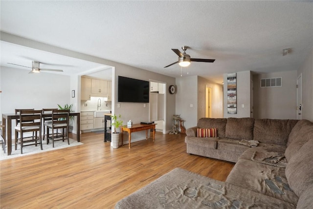 living room featuring light wood finished floors, visible vents, ceiling fan, a textured ceiling, and baseboards