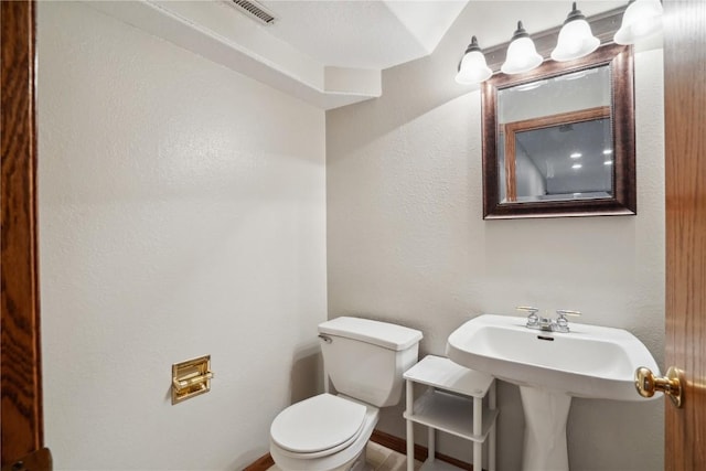 half bathroom with toilet, visible vents, and a sink