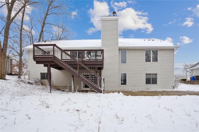 snow covered house featuring a deck, a chimney, and stairway