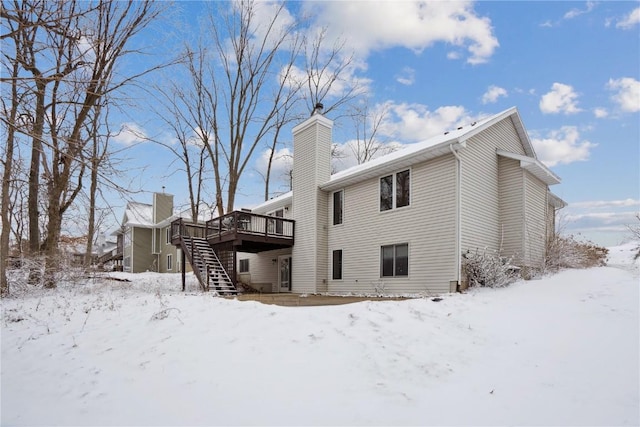 snow covered back of property with a chimney, stairway, and a wooden deck