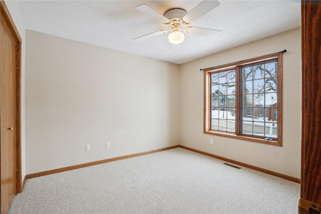 carpeted empty room featuring baseboards, a textured ceiling, visible vents, and a ceiling fan