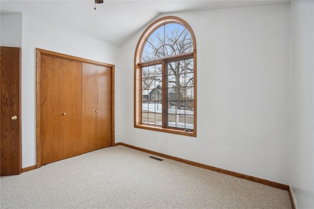 unfurnished bedroom featuring vaulted ceiling, multiple windows, carpet, and visible vents