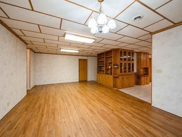 empty room with a paneled ceiling, light wood-style flooring, visible vents, and a notable chandelier