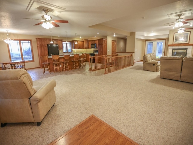 living area with a tile fireplace, light colored carpet, ceiling fan, and baseboards