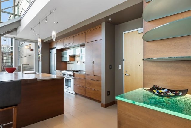 kitchen with stainless steel range, brown cabinets, hanging light fixtures, a sink, and track lighting