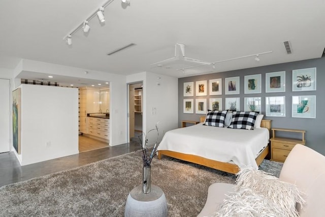 bedroom featuring visible vents, ensuite bath, a walk in closet, concrete flooring, and track lighting