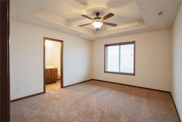 unfurnished bedroom featuring light colored carpet, a raised ceiling, visible vents, and baseboards