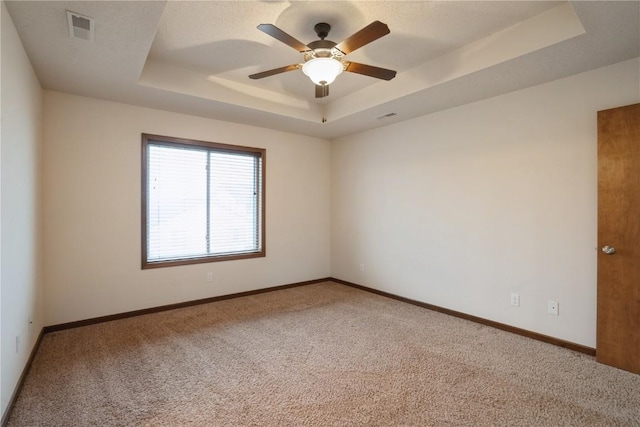 carpeted spare room with baseboards, visible vents, a raised ceiling, and a ceiling fan