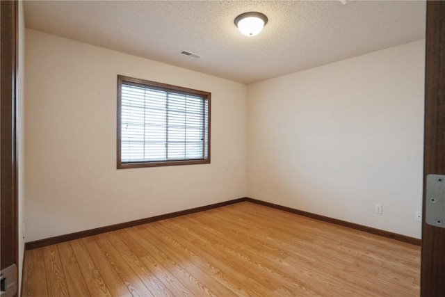 empty room featuring light wood-type flooring, visible vents, baseboards, and a textured ceiling