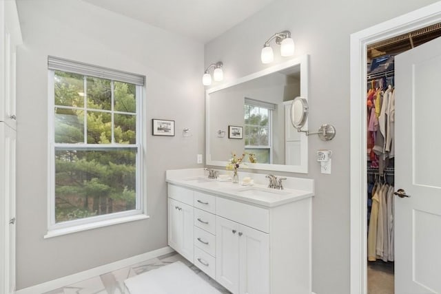 bathroom with marble finish floor, a sink, a spacious closet, and double vanity