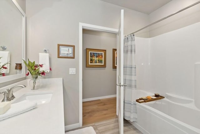 full bath with shower / tub combo, baseboards, wood finished floors, and vanity