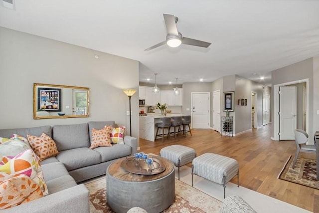 living area with light wood-style flooring, visible vents, ceiling fan, and baseboards