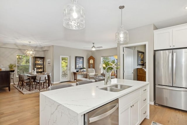 kitchen with light wood-style flooring, appliances with stainless steel finishes, a sink, and decorative light fixtures