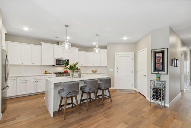 kitchen featuring a kitchen island with sink, stainless steel appliances, a kitchen breakfast bar, white cabinets, and light wood-style floors