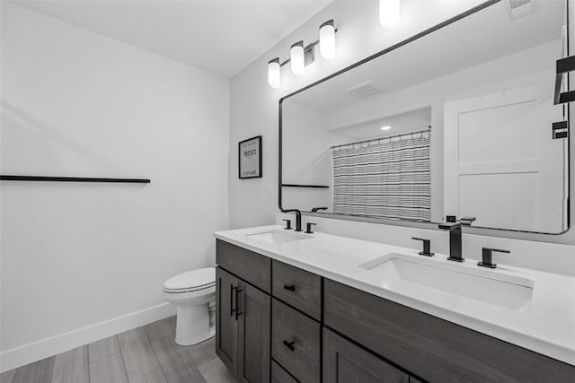 full bath with double vanity, a sink, toilet, and baseboards