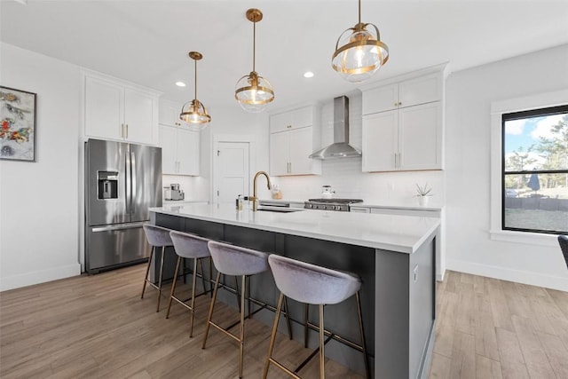 kitchen featuring tasteful backsplash, wall chimney exhaust hood, stove, light countertops, and stainless steel refrigerator with ice dispenser