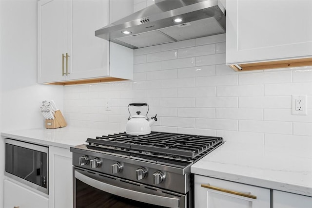 kitchen with white cabinetry, wall chimney range hood, appliances with stainless steel finishes, backsplash, and light stone countertops