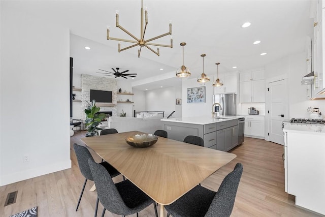 dining area with light wood-style floors, recessed lighting, visible vents, and a stone fireplace