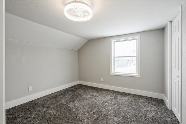 bonus room with dark colored carpet, lofted ceiling, and baseboards