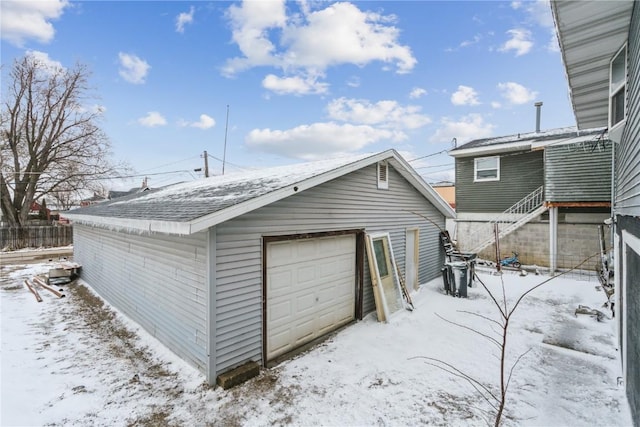 snow covered garage with a detached garage and fence