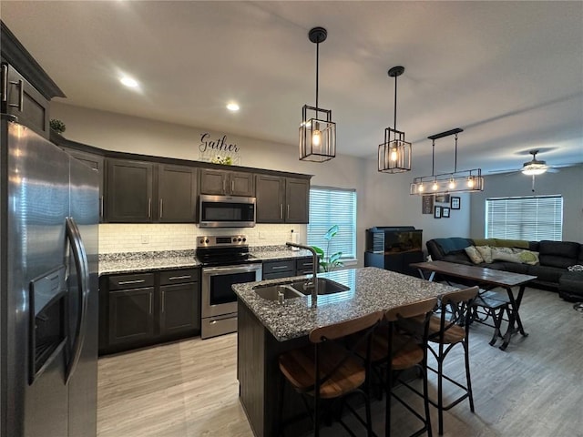 kitchen with stainless steel appliances, backsplash, open floor plan, a sink, and dark stone countertops