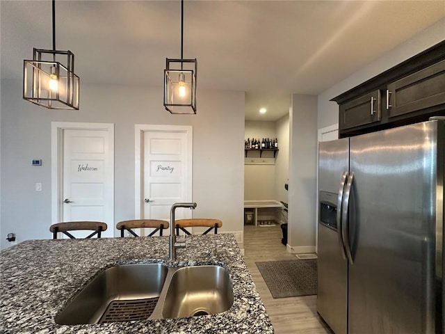 kitchen featuring light wood-style flooring, a sink, hanging light fixtures, dark stone counters, and stainless steel fridge