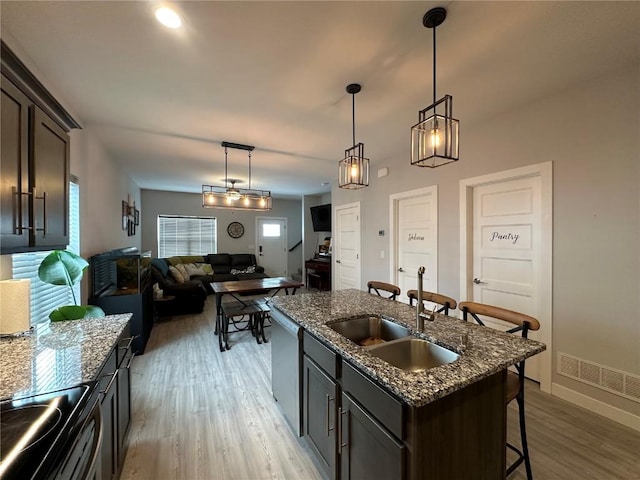 kitchen featuring visible vents, a sink, light wood-style floors, a kitchen bar, and stainless steel dishwasher