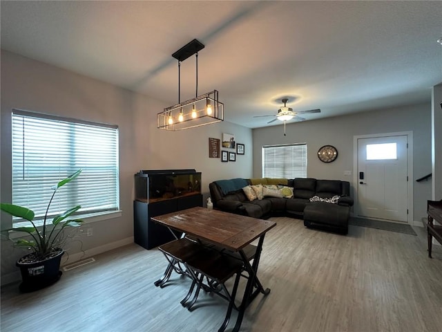 living area featuring light wood-style flooring, visible vents, baseboards, and ceiling fan