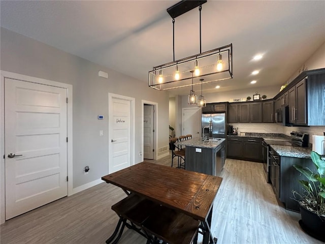 kitchen featuring appliances with stainless steel finishes, stone countertops, light wood-style floors, and an island with sink