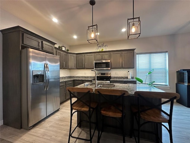 kitchen with stainless steel appliances, tasteful backsplash, light wood-style flooring, a sink, and dark stone countertops