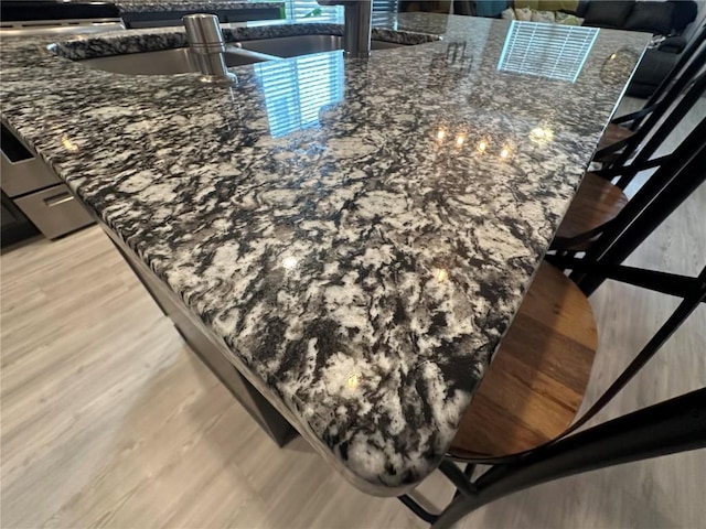 interior details with dark stone countertops, light wood-type flooring, a sink, and range