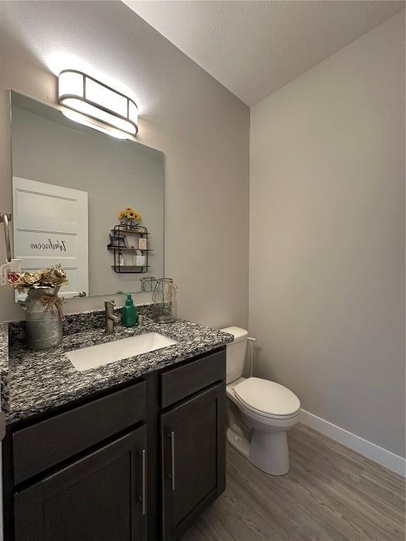 bathroom with toilet, wood finished floors, vanity, and baseboards