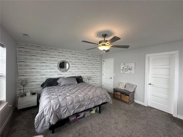 carpeted bedroom with ceiling fan, an accent wall, visible vents, and baseboards