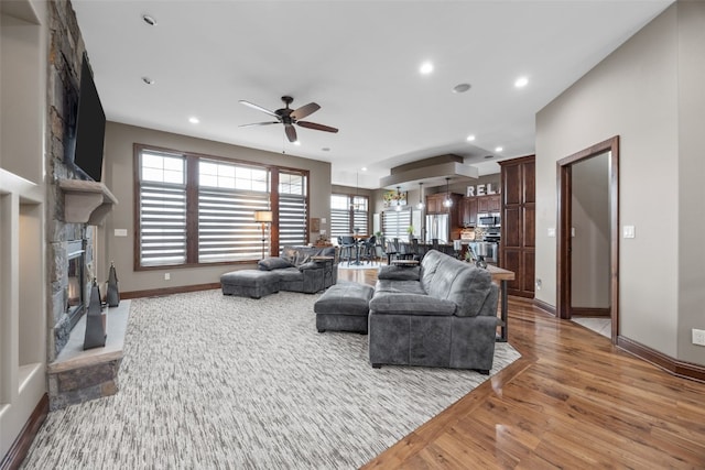 living area featuring baseboards, a ceiling fan, light wood-type flooring, a fireplace, and recessed lighting